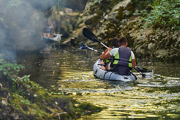 Image showing A group of friends enjoying having fun and kayaking while exploring the calm river, surrounding forest and large natural river canyons