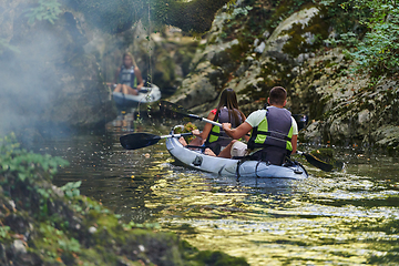 Image showing A group of friends enjoying having fun and kayaking while exploring the calm river, surrounding forest and large natural river canyons