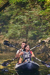 Image showing A young couple enjoying an idyllic kayak ride in the middle of a beautiful river surrounded by forest greenery