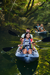 Image showing A group of friends enjoying having fun and kayaking while exploring the calm river, surrounding forest and large natural river canyons