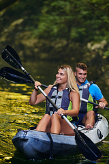 Image showing A young couple enjoying an idyllic kayak ride in the middle of a beautiful river surrounded by forest greenery