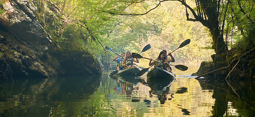 Image showing A group of friends enjoying having fun and kayaking while exploring the calm river, surrounding forest and large natural river canyons