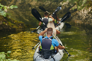 Image showing A group of friends enjoying having fun and kayaking while exploring the calm river, surrounding forest and large natural river canyons