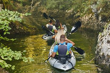 Image showing A group of friends enjoying having fun and kayaking while exploring the calm river, surrounding forest and large natural river canyons