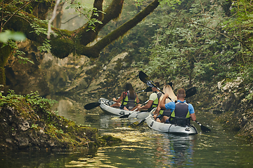 Image showing A group of friends enjoying having fun and kayaking while exploring the calm river, surrounding forest and large natural river canyons