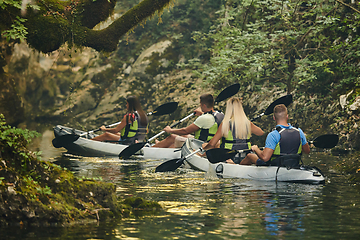 Image showing A group of friends enjoying having fun and kayaking while exploring the calm river, surrounding forest and large natural river canyons