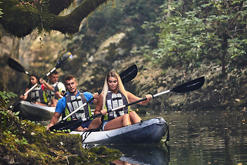 Image showing A group of friends enjoying having fun and kayaking while exploring the calm river, surrounding forest and large natural river canyons