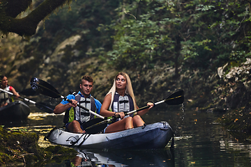 Image showing A group of friends enjoying having fun and kayaking while exploring the calm river, surrounding forest and large natural river canyons