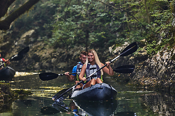 Image showing A group of friends enjoying having fun and kayaking while exploring the calm river, surrounding forest and large natural river canyons