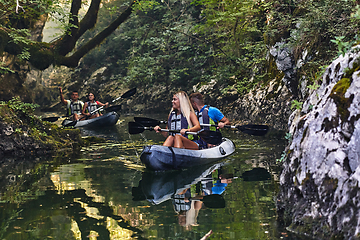 Image showing A group of friends enjoying having fun and kayaking while exploring the calm river, surrounding forest and large natural river canyons