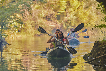 Image showing A group of friends enjoying having fun and kayaking while exploring the calm river, surrounding forest and large natural river canyons