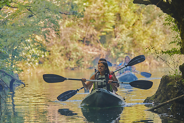 Image showing A group of friends enjoying having fun and kayaking while exploring the calm river, surrounding forest and large natural river canyons