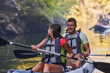 Image showing A group of friends enjoying having fun and kayaking while exploring the calm river, surrounding forest and large natural river canyons