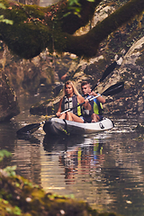 Image showing A young couple enjoying an idyllic kayak ride in the middle of a beautiful river surrounded by forest greenery