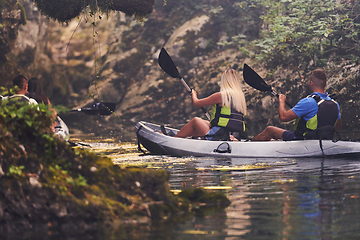 Image showing A young couple enjoying an idyllic kayak ride in the middle of a beautiful river surrounded by forest greenery