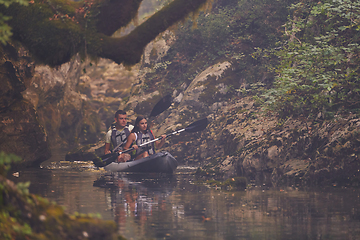 Image showing A young couple enjoying an idyllic kayak ride in the middle of a beautiful river surrounded by forest greenery