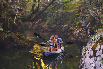 Image showing A young couple enjoying an idyllic kayak ride in the middle of a beautiful river surrounded by forest greenery