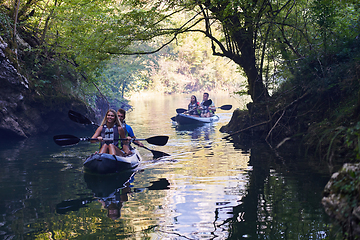 Image showing A group of friends enjoying having fun and kayaking while exploring the calm river, surrounding forest and large natural river canyons