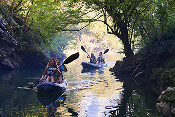 Image showing A group of friends enjoying having fun and kayaking while exploring the calm river, surrounding forest and large natural river canyons