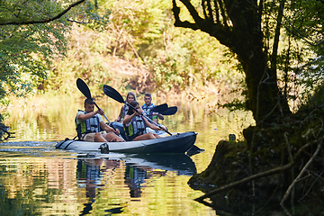 Image showing A group of friends enjoying having fun and kayaking while exploring the calm river, surrounding forest and large natural river canyons