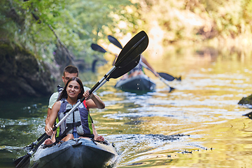 Image showing A group of friends enjoying having fun and kayaking while exploring the calm river, surrounding forest and large natural river canyons