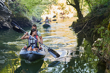 Image showing A group of friends enjoying having fun and kayaking while exploring the calm river, surrounding forest and large natural river canyons