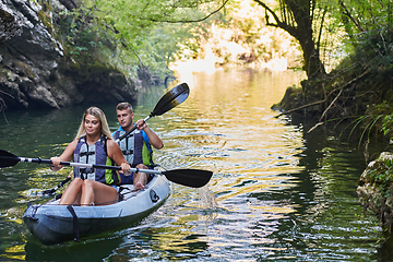 Image showing A group of friends enjoying having fun and kayaking while exploring the calm river, surrounding forest and large natural river canyons