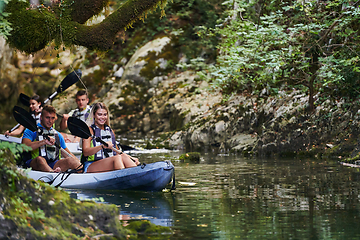 Image showing A group of friends enjoying having fun and kayaking while exploring the calm river, surrounding forest and large natural river canyons