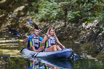 Image showing A young couple enjoying an idyllic kayak ride in the middle of a beautiful river surrounded by forest greenery