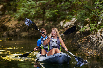 Image showing A young couple enjoying an idyllic kayak ride in the middle of a beautiful river surrounded by forest greenery