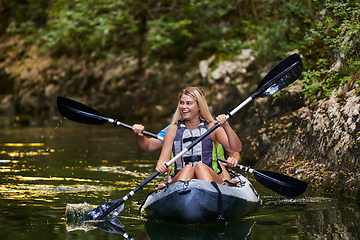 Image showing A young couple enjoying an idyllic kayak ride in the middle of a beautiful river surrounded by forest greenery