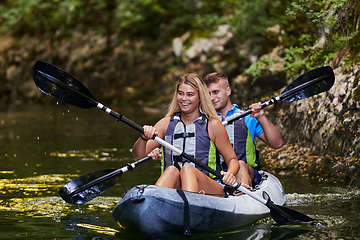 Image showing A young couple enjoying an idyllic kayak ride in the middle of a beautiful river surrounded by forest greenery