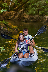 Image showing A young couple enjoying an idyllic kayak ride in the middle of a beautiful river surrounded by forest greenery