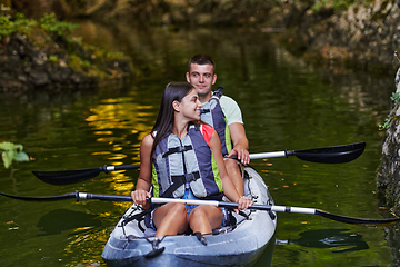Image showing A young couple enjoying an idyllic kayak ride in the middle of a beautiful river surrounded by forest greenery