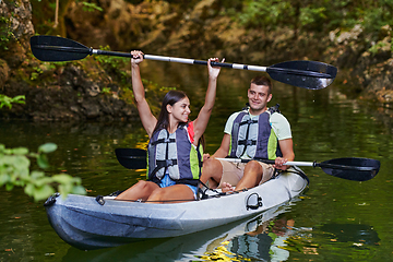 Image showing A young couple enjoying an idyllic kayak ride in the middle of a beautiful river surrounded by forest greenery