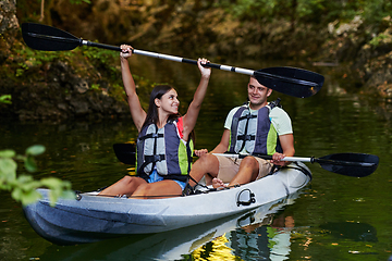 Image showing A young couple enjoying an idyllic kayak ride in the middle of a beautiful river surrounded by forest greenery