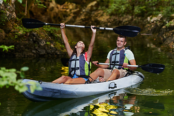 Image showing A young couple enjoying an idyllic kayak ride in the middle of a beautiful river surrounded by forest greenery