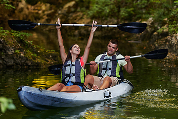 Image showing A young couple enjoying an idyllic kayak ride in the middle of a beautiful river surrounded by forest greenery