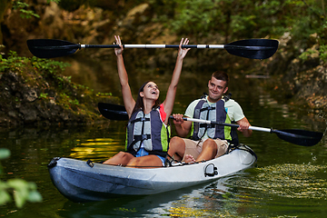 Image showing A young couple enjoying an idyllic kayak ride in the middle of a beautiful river surrounded by forest greenery