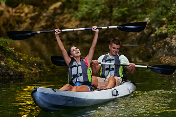 Image showing A young couple enjoying an idyllic kayak ride in the middle of a beautiful river surrounded by forest greenery