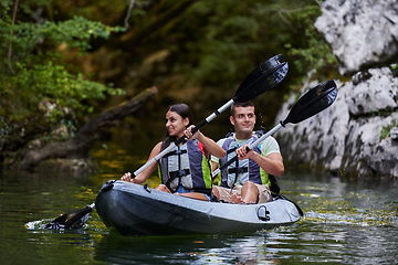 Image showing A young couple enjoying an idyllic kayak ride in the middle of a beautiful river surrounded by forest greenery