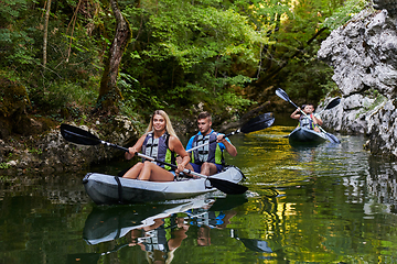 Image showing A group of friends enjoying having fun and kayaking while exploring the calm river, surrounding forest and large natural river canyons