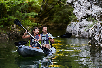 Image showing A young couple enjoying an idyllic kayak ride in the middle of a beautiful river surrounded by forest greenery