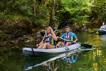 Image showing A group of friends enjoying having fun and kayaking while exploring the calm river, surrounding forest and large natural river canyons