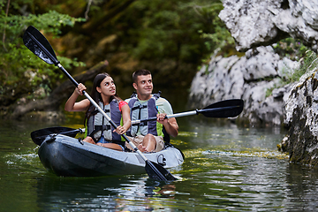 Image showing A young couple enjoying an idyllic kayak ride in the middle of a beautiful river surrounded by forest greenery