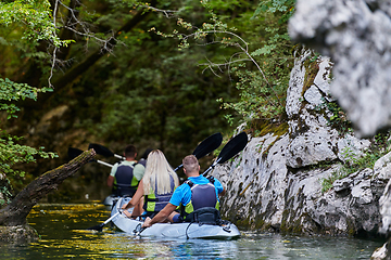 Image showing A group of friends enjoying having fun and kayaking while exploring the calm river, surrounding forest and large natural river canyons