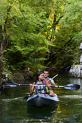 Image showing A young couple enjoying an idyllic kayak ride in the middle of a beautiful river surrounded by forest greenery