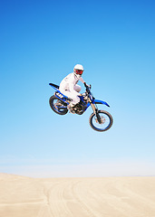 Image showing Jump, motorbike and person in desert, blue sky with action and extreme sport, speed outdoor and mockup space. Adventure, fitness and motorcycle in air with stunt performance, freedom and challenge