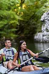 Image showing A young couple enjoying an idyllic kayak ride in the middle of a beautiful river surrounded by forest greenery