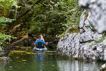 Image showing A young couple enjoying an idyllic kayak ride in the middle of a beautiful river surrounded by forest greenery